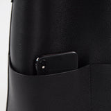 Black cowhide leather tote bag with front pocket holding a smartphone, minimalist design