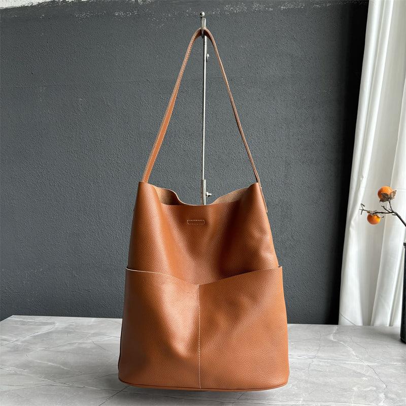 Brown cowhide leather tote bag with two front pockets, minimalist style, on marble table.
