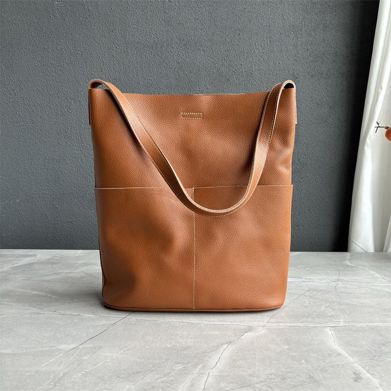 Brown cowhide leather tote bag with two front pockets on a marble surface