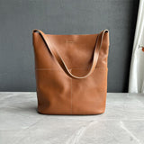 Brown cowhide leather tote bag with two front pockets on a marble surface