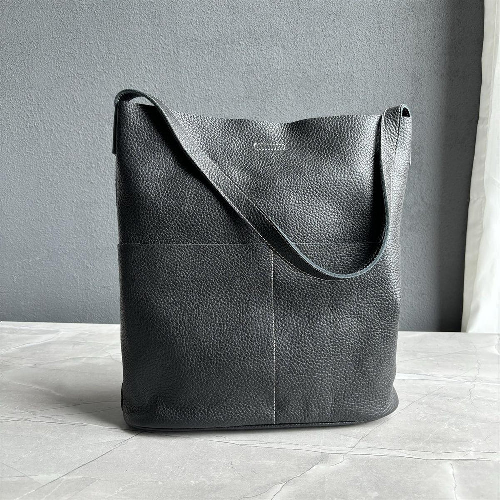 Black cowhide leather tote bag with two front pockets, minimalist design, on marble surface