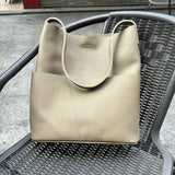 Soft tan cowhide leather tote bag with two front pockets on a wicker chair outdoors