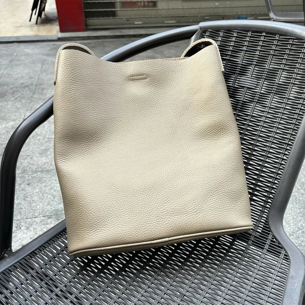 Beige cowhide leather tote bag with minimalist design placed on a black outdoor chair