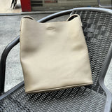 Beige cowhide leather tote bag with minimalist design placed on a black outdoor chair