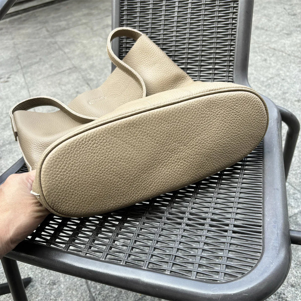 Taupe cowhide leather tote bag with pebble texture, shown on an outdoor metal chair.