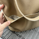 Hand holding open front pocket of taupe cowhide leather tote bag with textured finish