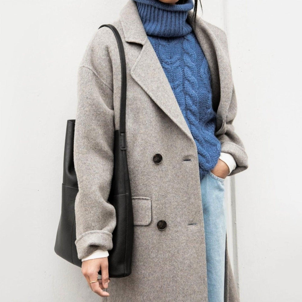 Woman wearing a grey coat and blue sweater carrying a black leather tote bag