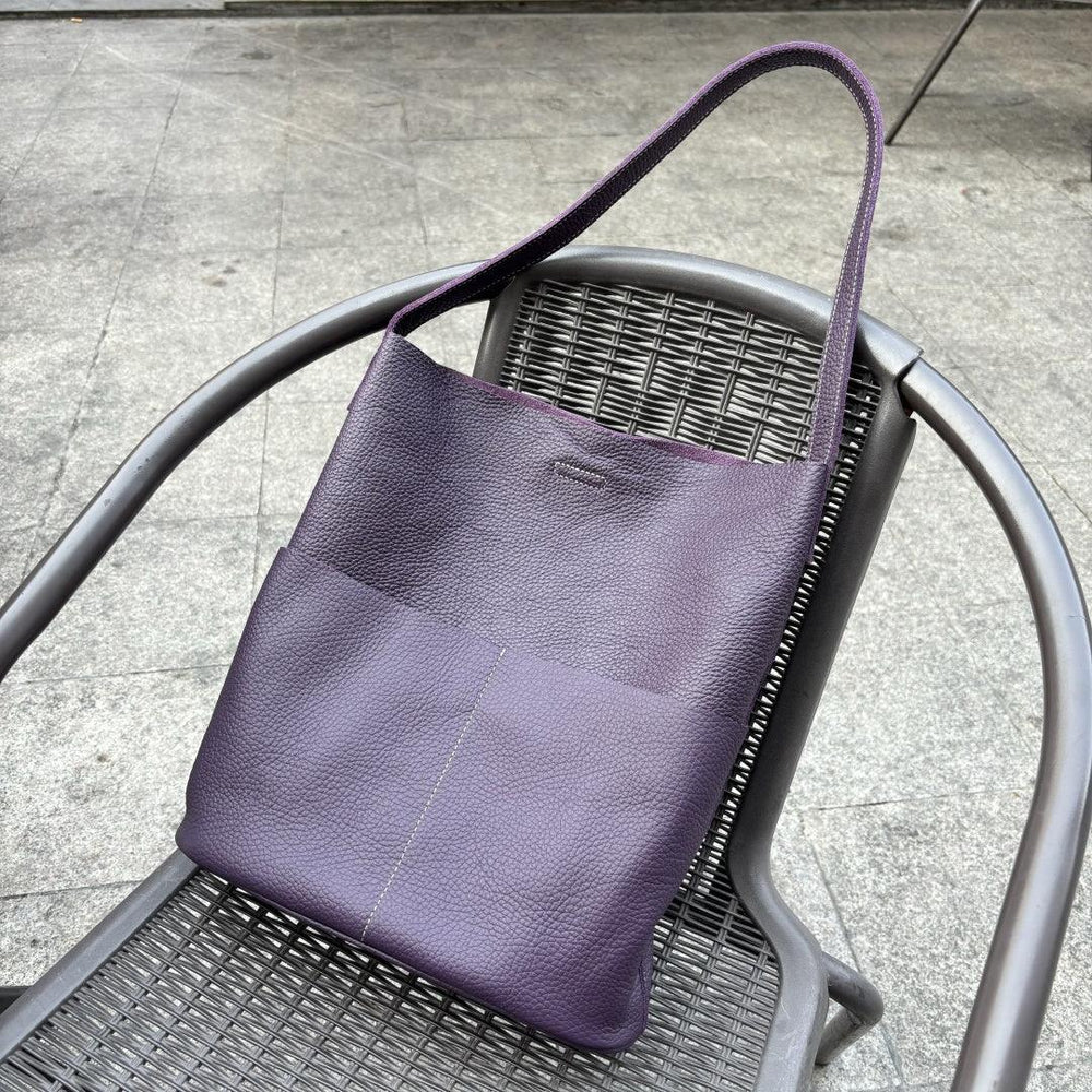 Purple cowhide leather tote bag with front pockets on a metal chair outdoors