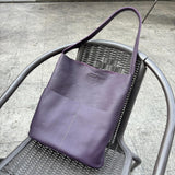 Purple cowhide leather tote bag with front pockets on a metal chair outdoors