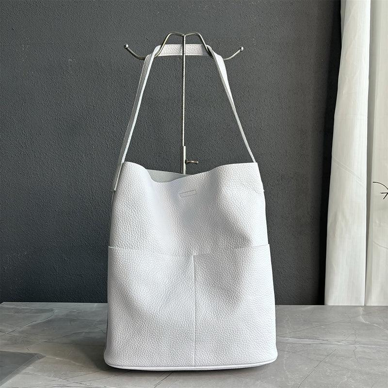 White cowhide leather tote bag with front pockets and minimalist bucket design on marble surface