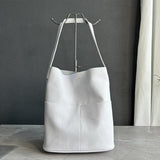 White cowhide leather tote bag with front pockets and minimalist bucket design on marble surface