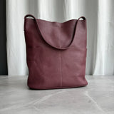 Brown cowhide leather tote bag with two front pockets on marble surface, minimalist design
