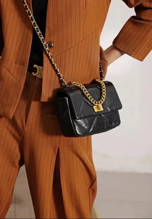 Black quilted leather shoulder bag with gold chain strap and lock, worn over an orange suit