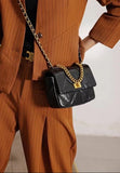 Black quilted leather shoulder bag with gold chain strap and lock, worn over an orange suit