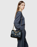 Woman wearing a black quilted leather shoulder bag with gold chain strap and turn-lock clasp