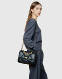 Woman wearing a black quilted leather shoulder bag with gold chain strap and turn-lock clasp