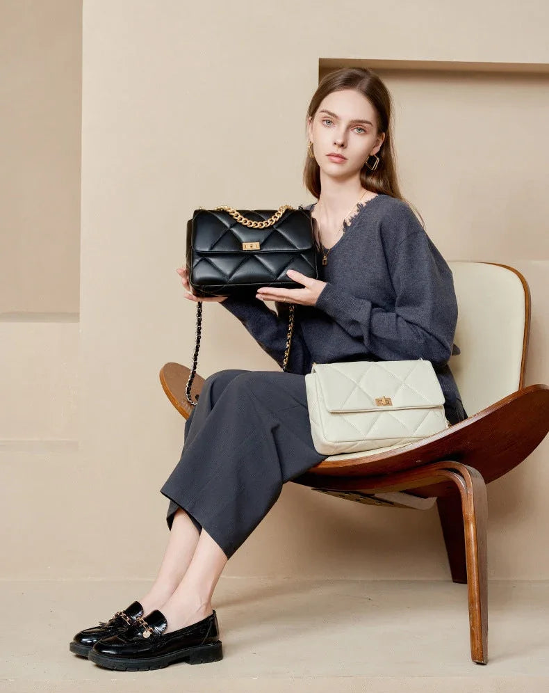 Woman seated holding a black quilted leather shoulder bag with gold chain, cream quilted bag on lap