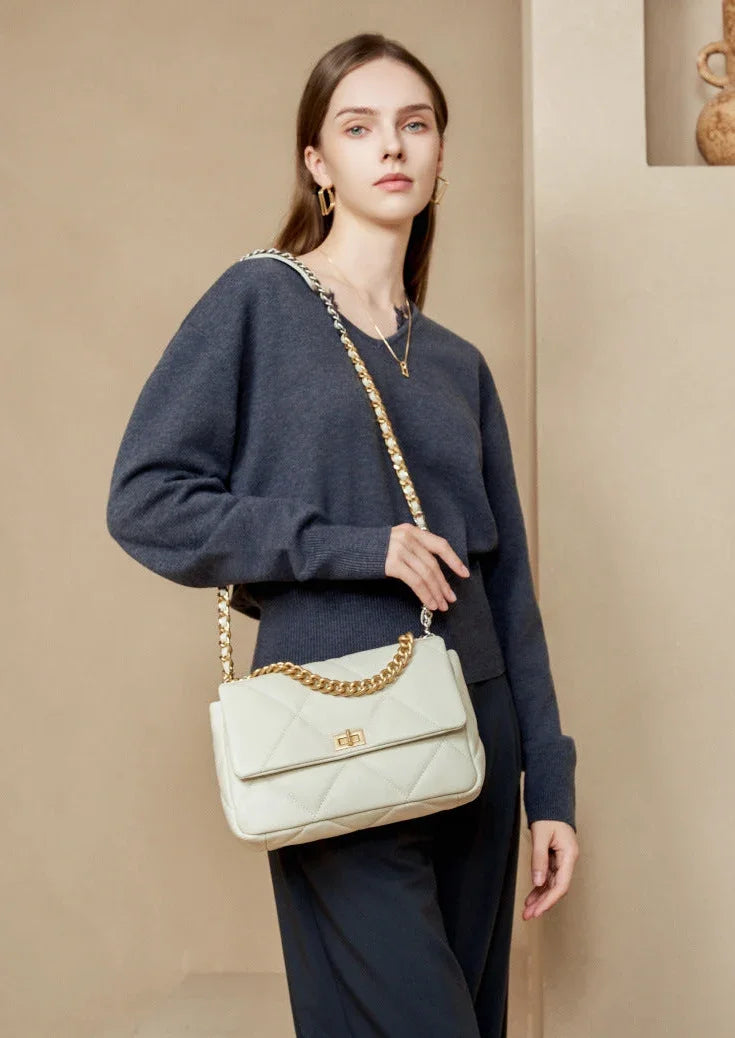 Woman wearing a quilted leather shoulder bag with gold chain strap and turn-lock closure