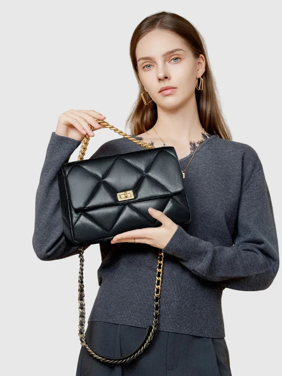 Woman holding a black quilted genuine leather shoulder bag with gold chain strap and lock.