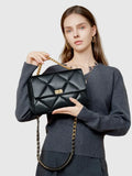 Woman holding a black quilted genuine leather shoulder bag with gold chain strap and lock.