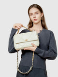 Woman holding a cream quilted leather shoulder bag with gold chain strap and turn-lock clasp