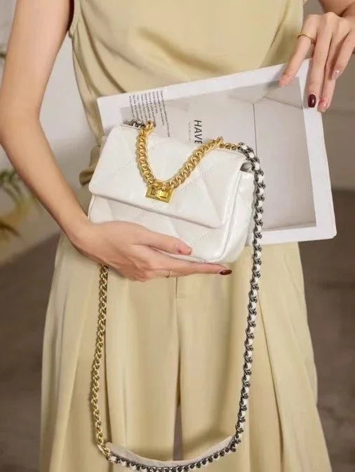 White quilted leather shoulder bag with gold chain strap and lock, held by woman in beige outfit