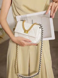 White quilted leather shoulder bag with gold chain strap and lock, held by woman in beige outfit
