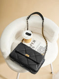 Black quilted leather shoulder bag with gold chain strap on white chair, next to coffee cup and magazine