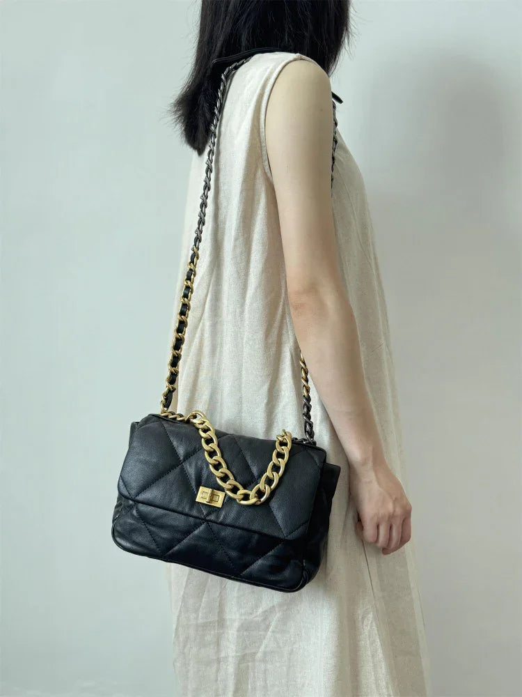 Woman carrying a black quilted leather shoulder bag with gold chain strap and lock clasp
