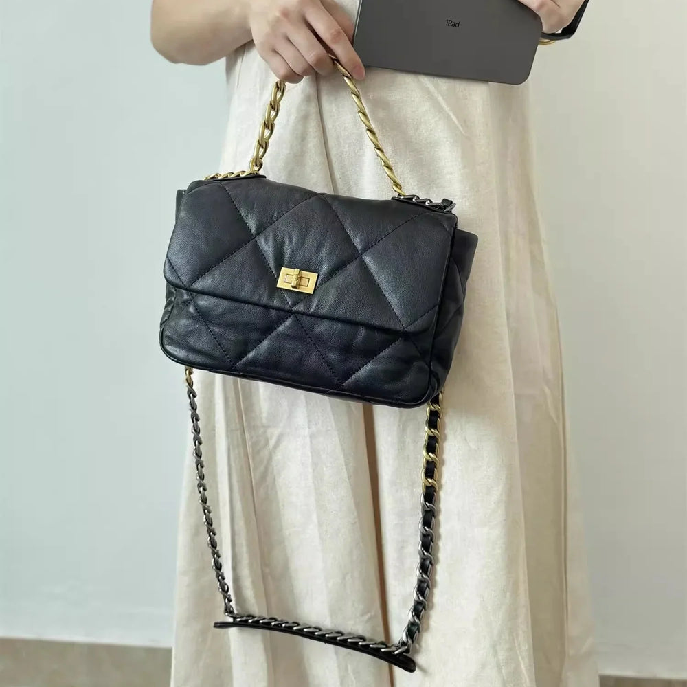 Black quilted leather shoulder bag with gold chain strap and turn-lock clasp, held by woman