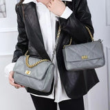 Woman in black blazer holding two grey quilted genuine leather shoulder bags with gold chains
