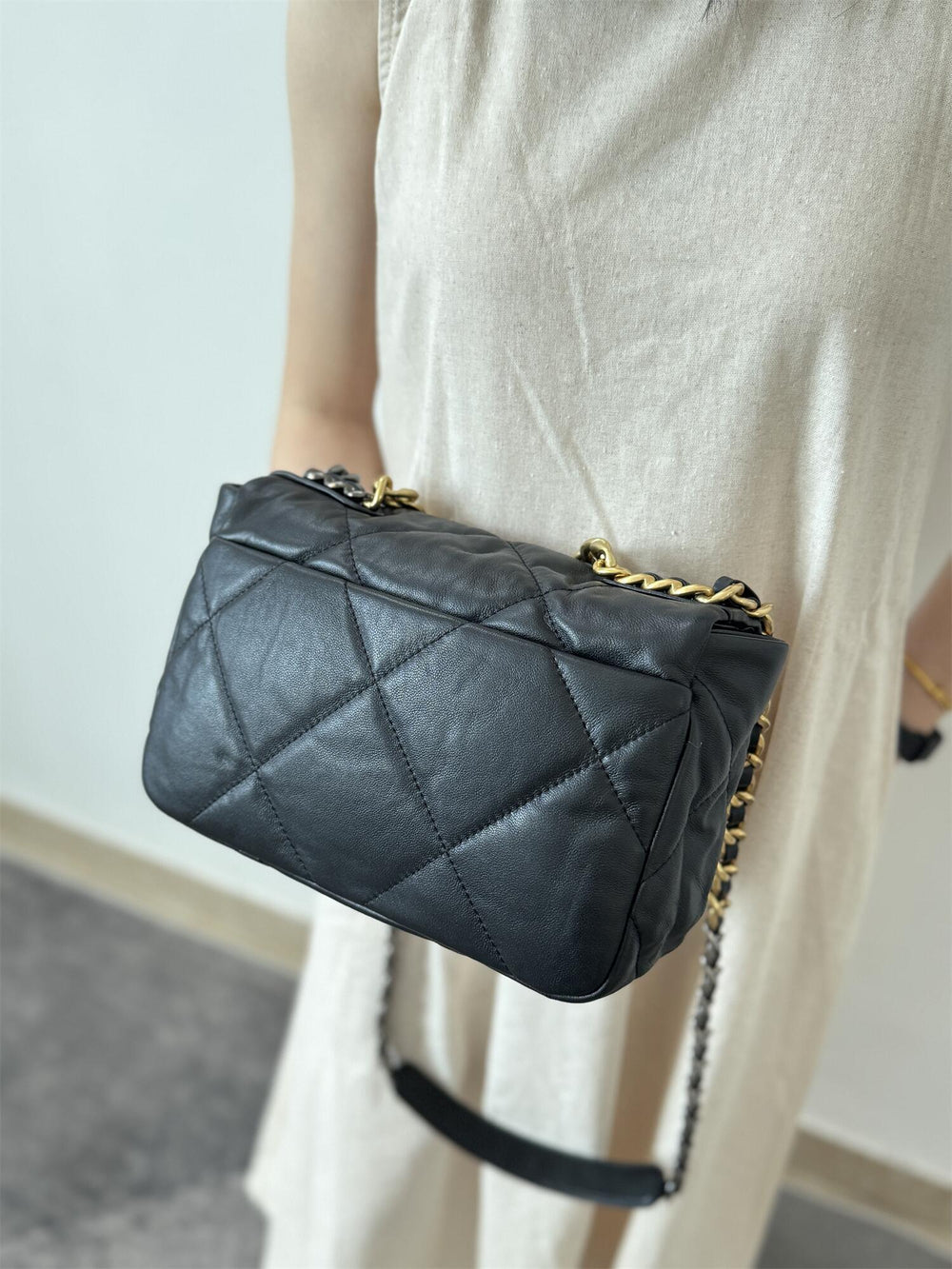 Black quilted leather shoulder bag with gold chain strap, crossbody style, worn by woman