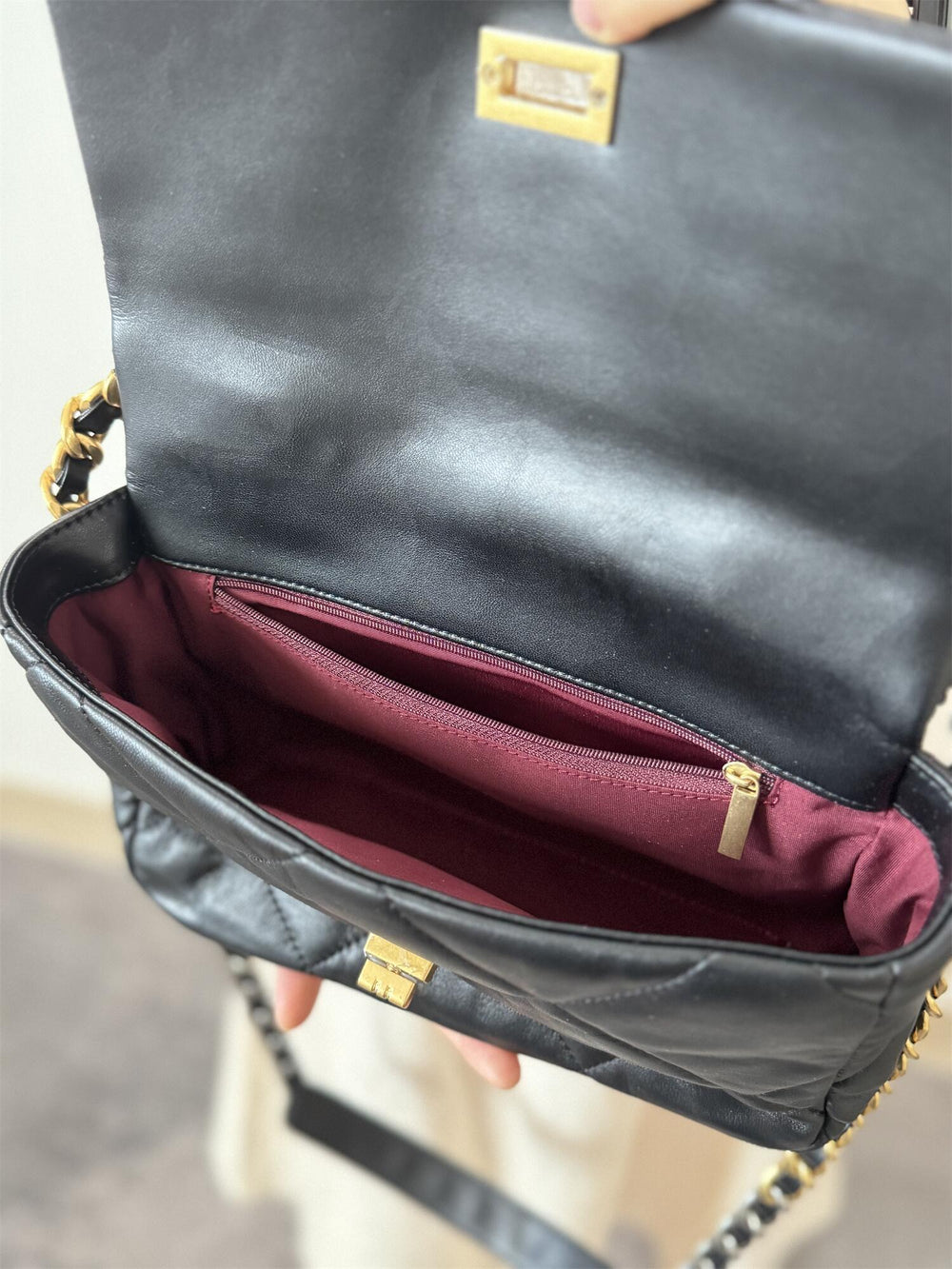 Open black quilted leather shoulder bag with gold chain strap, burgundy interior, and zip pocket.