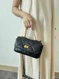 Black quilted leather shoulder bag with gold chain strap and turn-lock clasp held by a woman in a beige dress