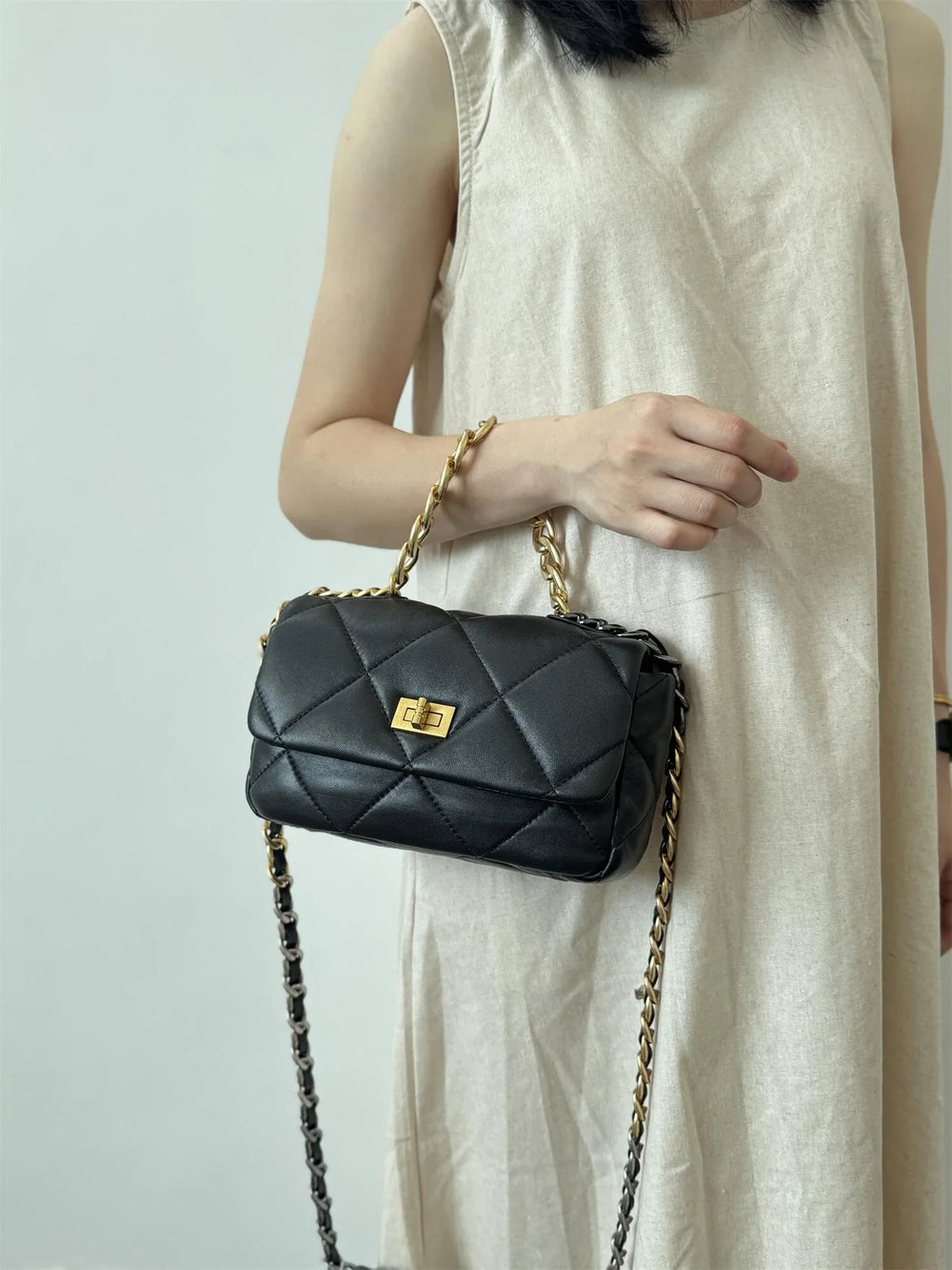Woman holding a black quilted leather shoulder bag with gold chain strap and turn-lock closure