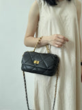 Woman holding a black quilted leather shoulder bag with gold chain strap and turn-lock closure