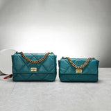 Teal quilted leather shoulder bags with gold chain strap and clasp on marble surface