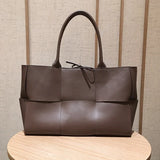 Quilted large brown leather tote bag with top handles on a wooden table, minimalist style.
