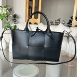 Black quilted leather tote bag with top handles and shoulder strap on glass table in living room