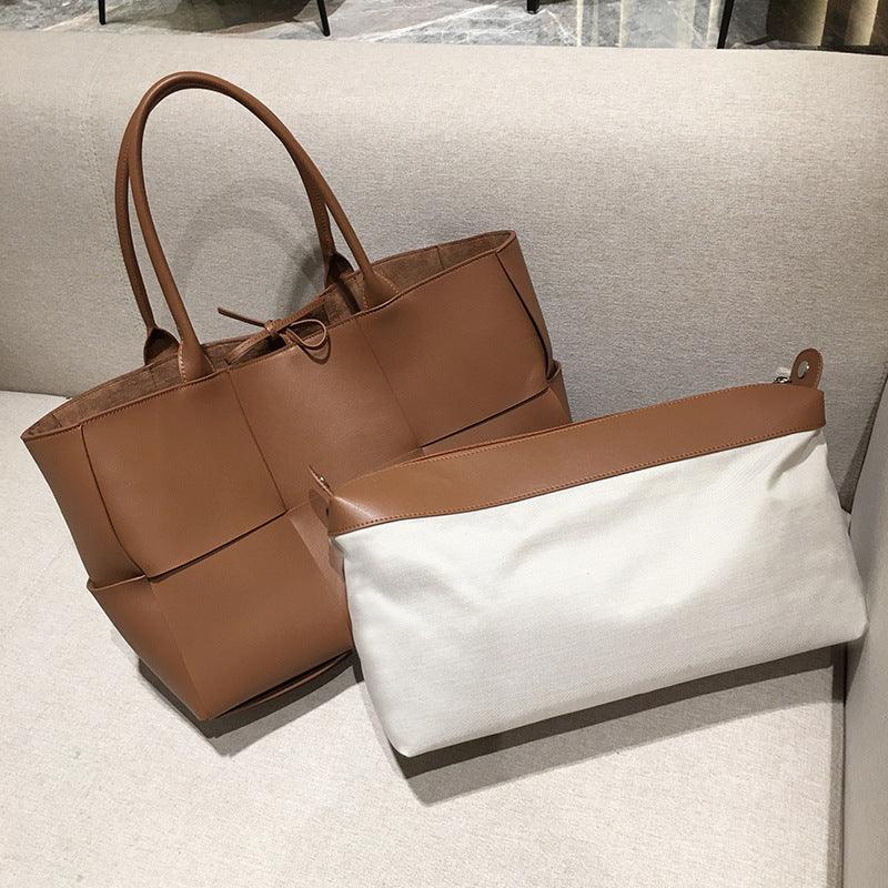 Large tan leather tote bag with top handles and matching beige pouch on a sofa