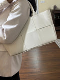 Woman carrying a large white quilted leather tote bag with woven texture and top handles.