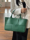 Woman holding large green quilted leather tote bag with top handles, minimalist design