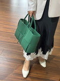 Woman holding green quilted leather tote bag with top handles, wearing lace-trimmed skirt and white heels