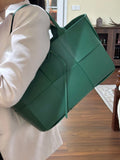 Woman carrying a large green leather tote bag with woven minimalist design and top handles