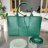Green quilted leather tote bag with top handles and detachable strap on a modern table.