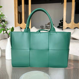 Large green woven leather tote bag with top handles on a glass table in a modern living room.