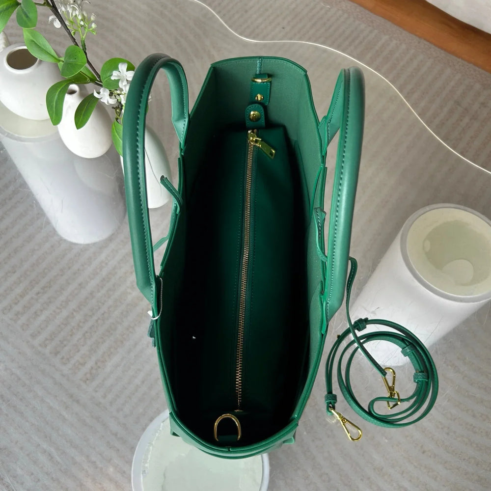 Green leather tote bag with top handles, gold zipper, and detachable shoulder strap on a table.