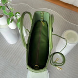 Green leather tote bag with top handle, interior zipper pouch, and detachable strap on a glass table.