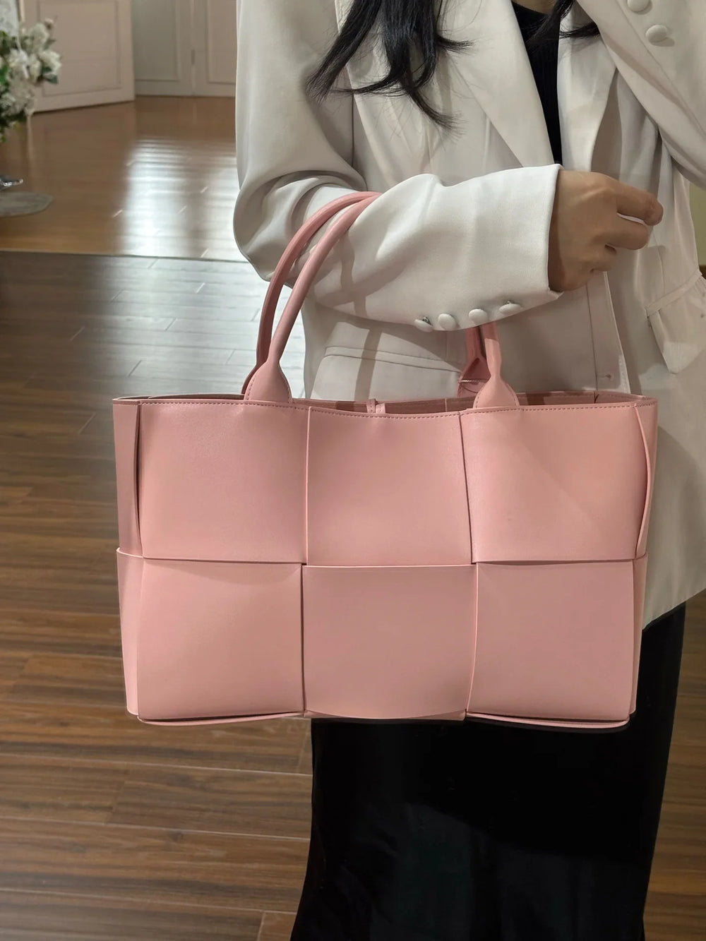 Woman carrying a large pink quilted leather tote bag with top handles, minimalist design