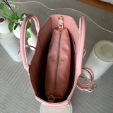Pink leather tote bag with top handle, gold zipper pouch, and detachable strap on glass table